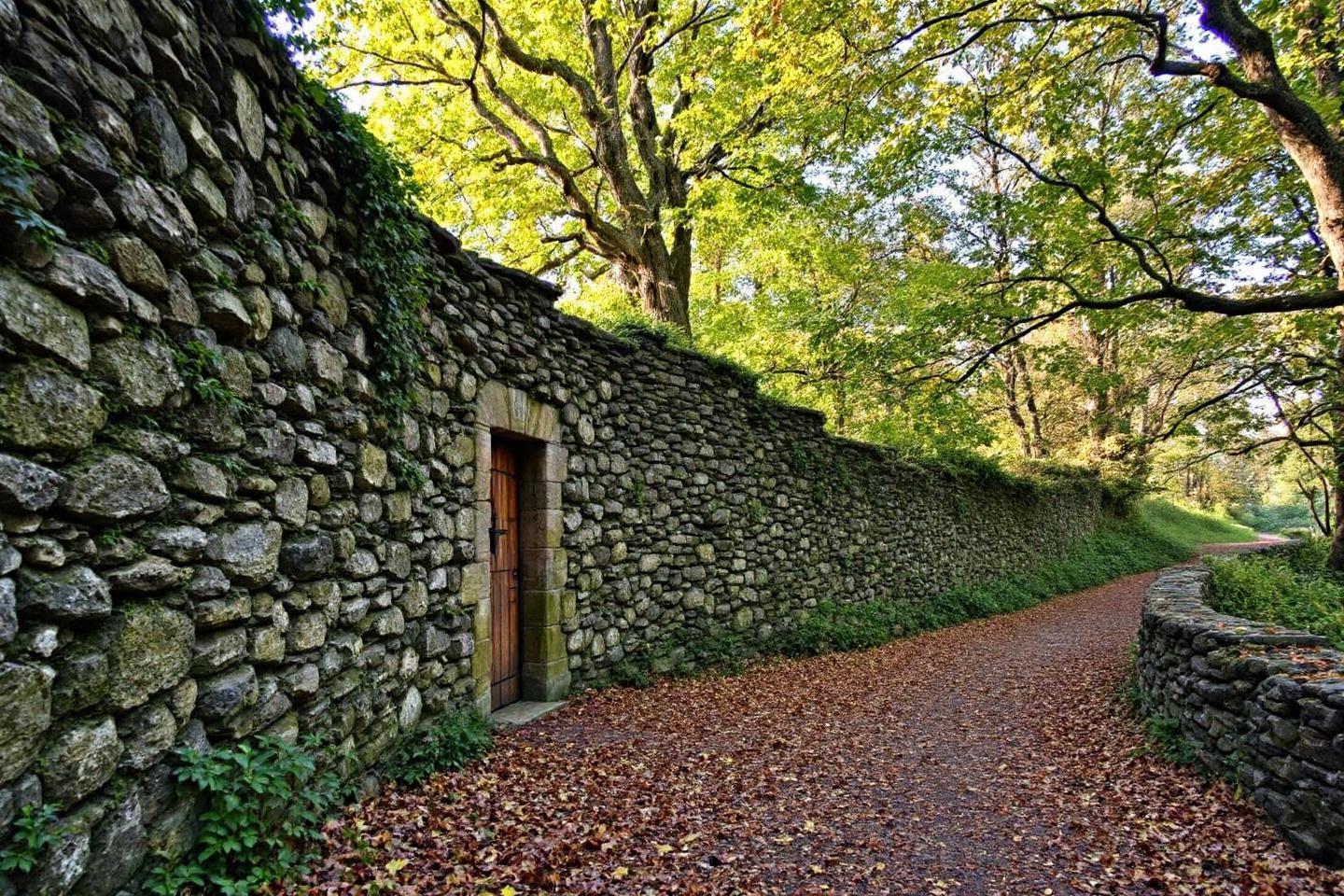 Sentier bordé de murs en pierre avec porte et arbres