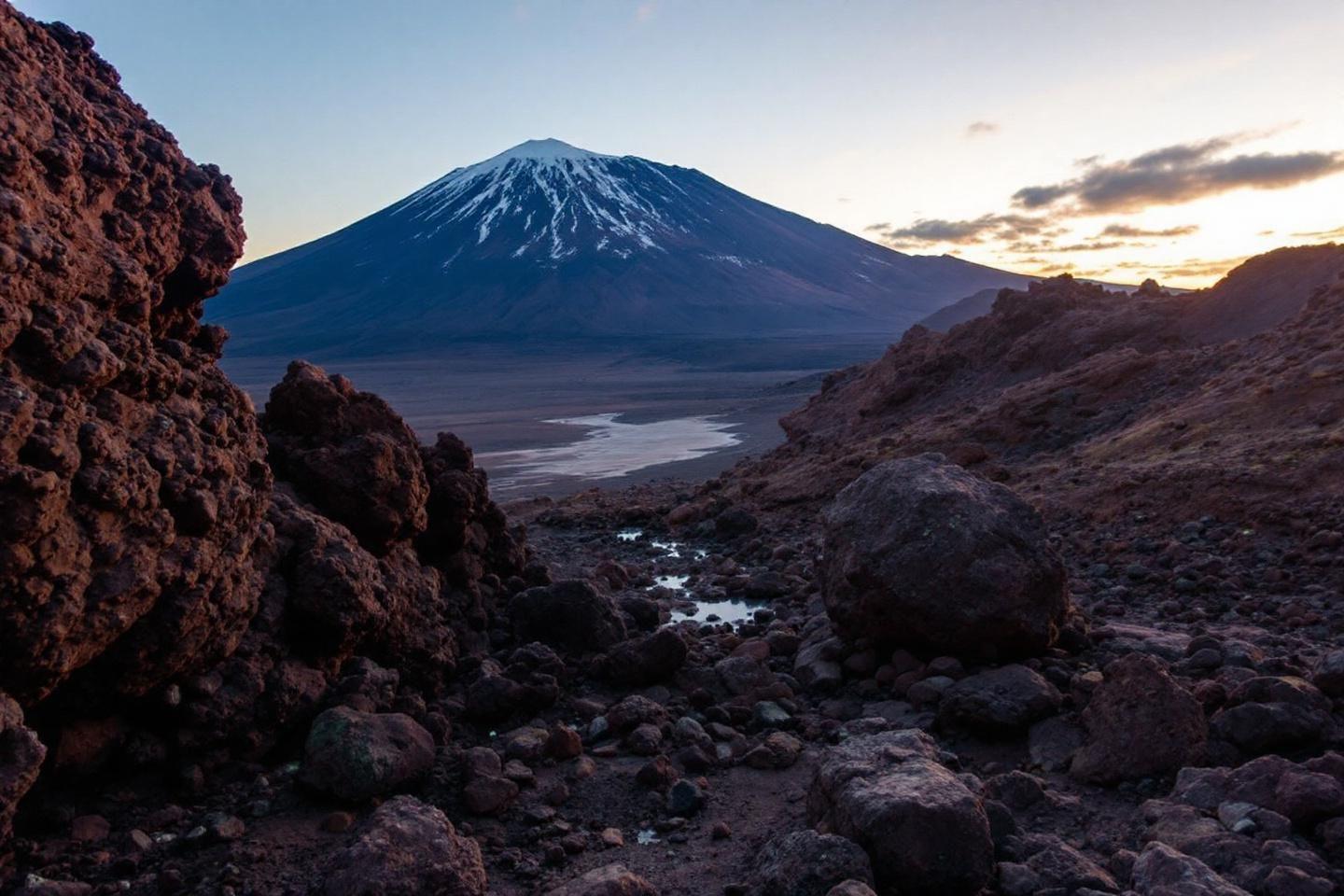 Volcan conique enneigé surplombant une vallée rocheuse