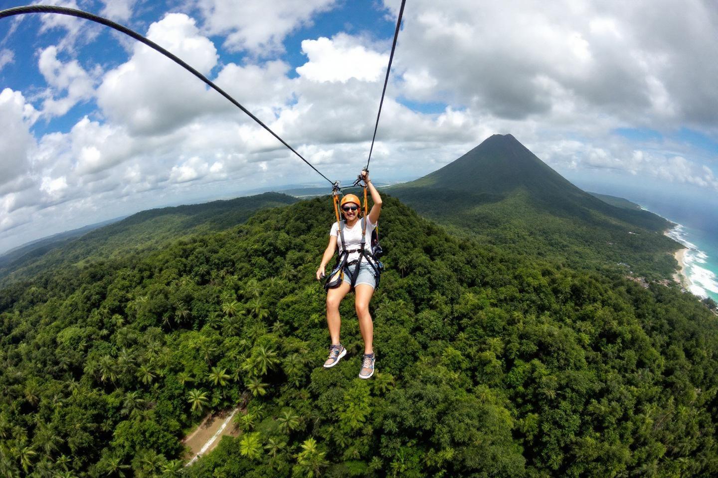 Vue aérienne d'une personne en tyrolienne survolant une jungle verdoyante